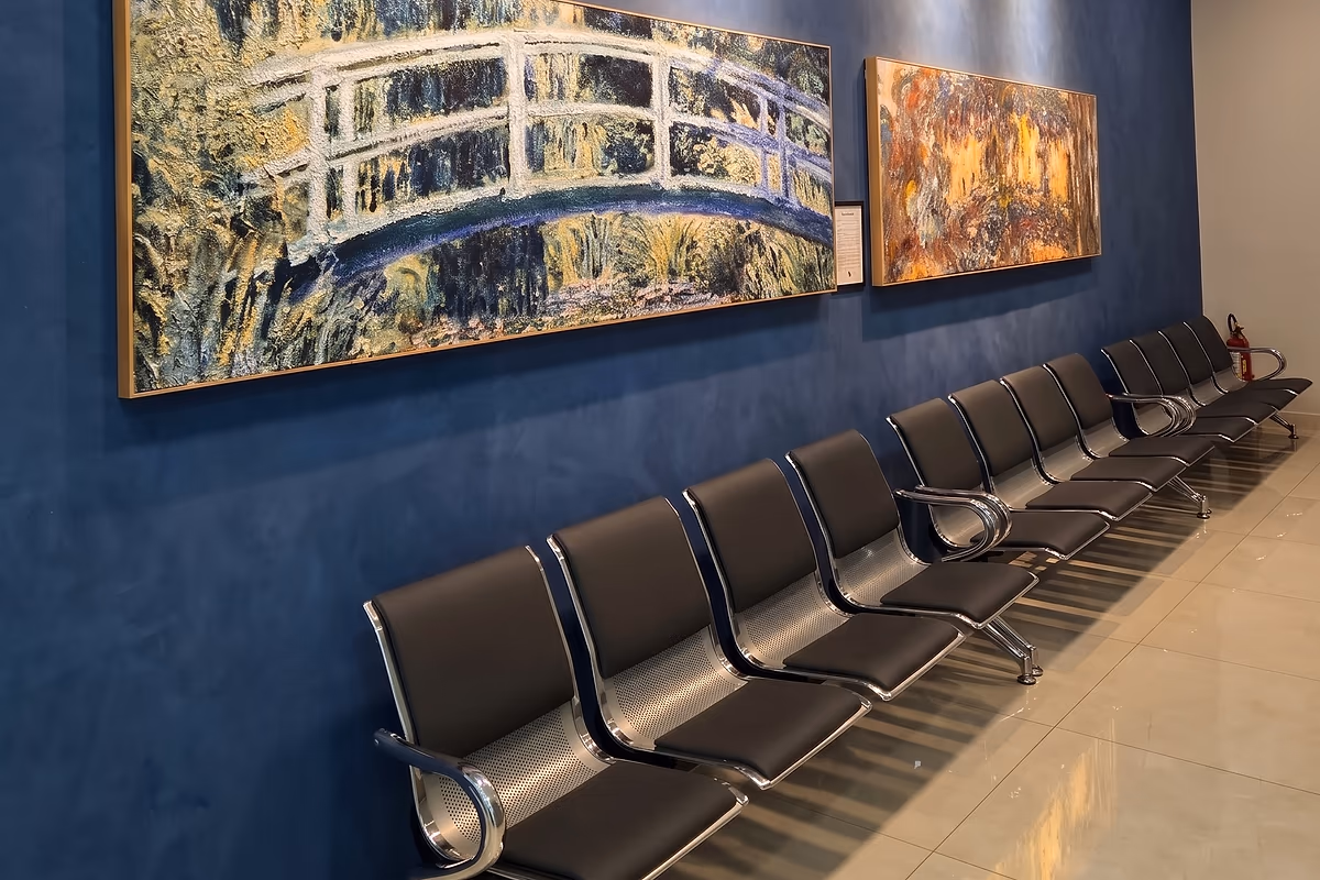 Fileira de poltronas sob duas reproduções de Claude Monet na parede azul da sala de espera