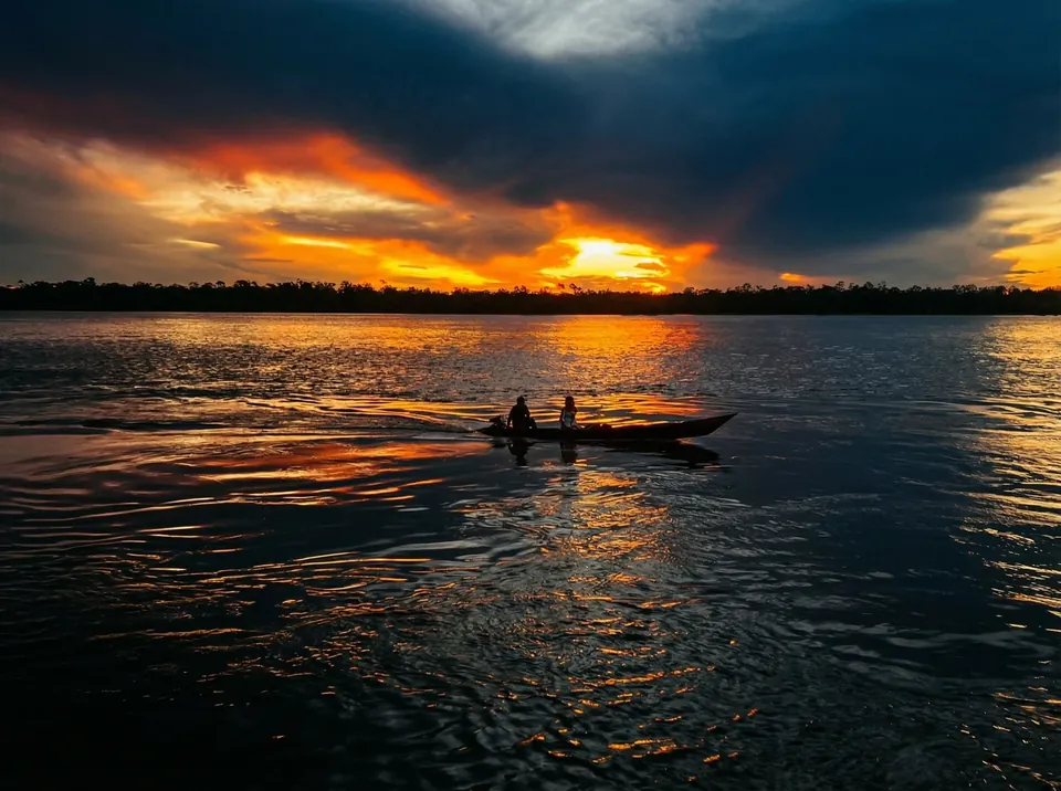 Pôr do sol no rio, com uma canoa ao longe
