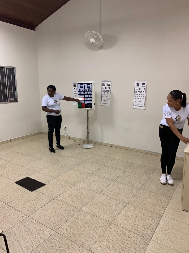 Duas profissionais de camiseta com o logotipo da rede numa sala com as tabelas de letras do exame de visão na parede