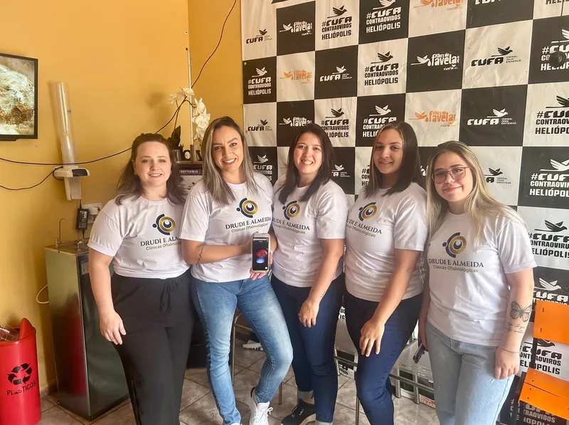 Cinco pessoas da equipe, de camiseta branca com o logotipo da rede, na sala com o painel da CUFA Heliópolis ao fundo