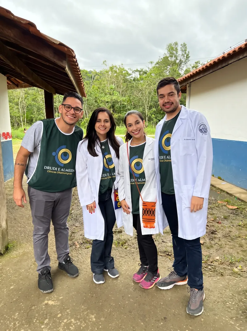 Quatro pessoas da equipe, de jaleco e colete verde com o logotipo da rede, na varanda da escola da aldeia