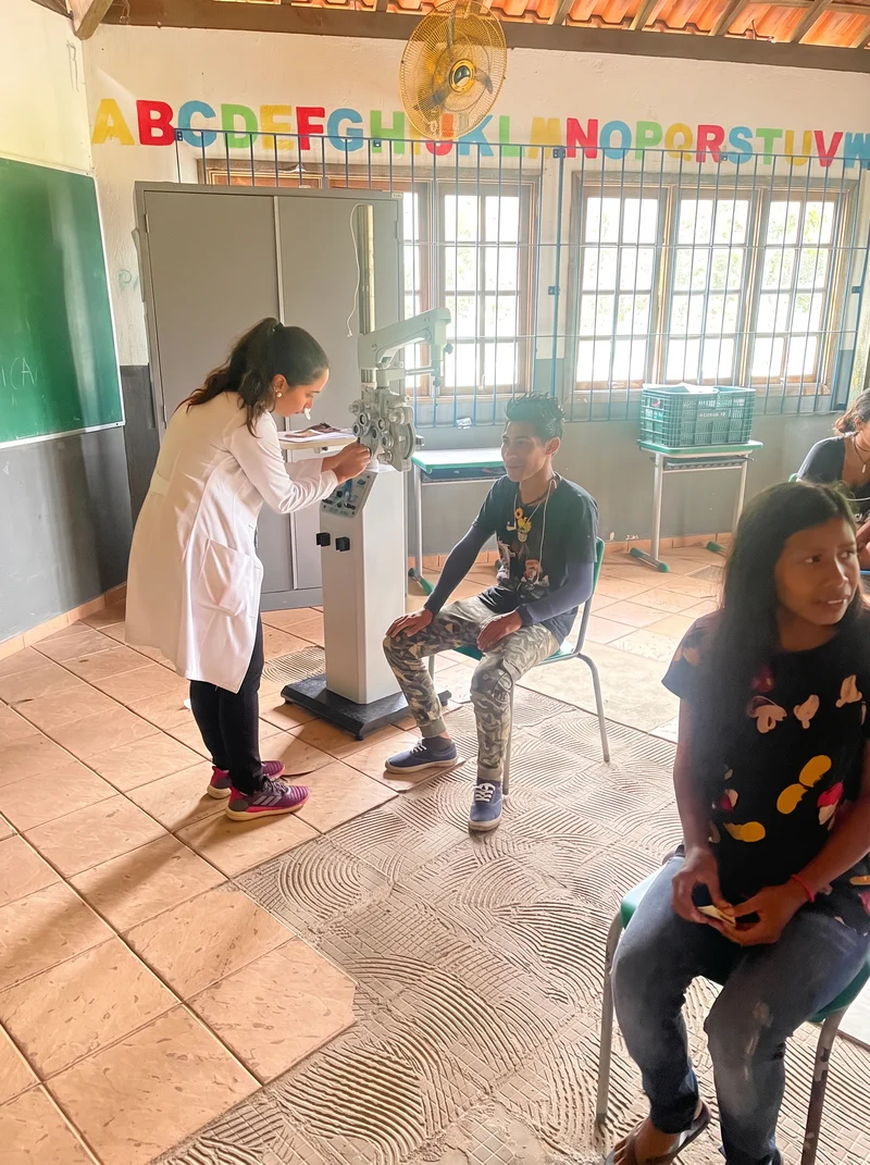 Profissional realizando exame de refração com foróptero em jovem indígena na escola da aldeia